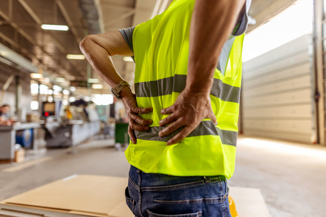 Warehouse worker experiencing lower back pain while lifting heavy boxes on the job.