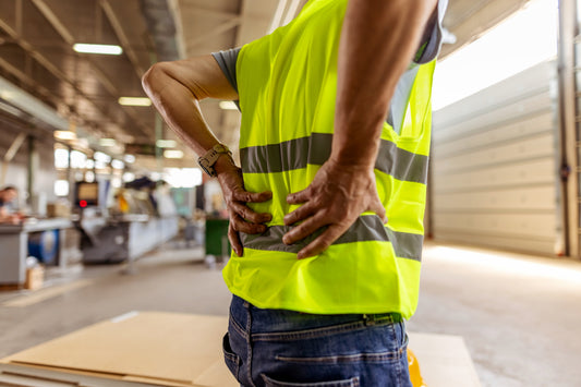 Warehouse worker experiencing lower back pain while lifting heavy boxes on the job.