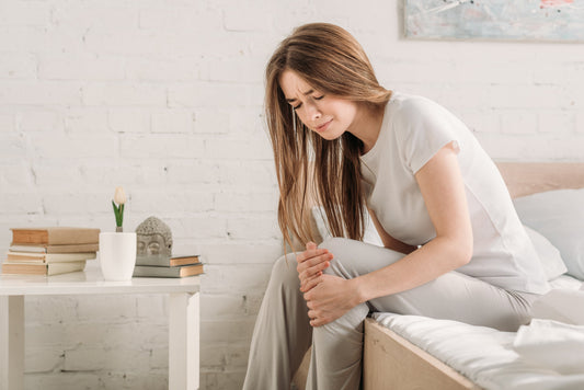Woman sitting on bed, grimacing and holding her painful knee.
