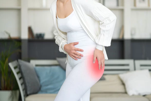Woman in white outfit holding her hip with red inflammation highlight on sacroiliac joint area indicating SI joint pain from standing or movement