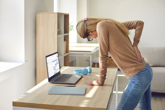 Woman hunching over a standing desk holding her lower back in pain from prolonged standing without anti-fatigue mat support