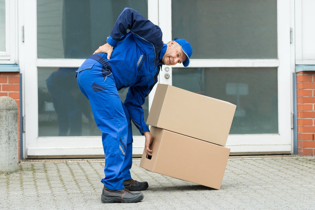 Delivery worker in pain bending over heavy boxes, highlighting lower back strain risk.