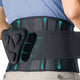Close-up rear view of FEATOL back brace worn on lower back, showing dual-direction compression arrows, breathable mesh panel, and ergonomic 3D lumbar pad partially pulled out to reveal foam cushion structure