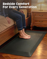 Person resting bare feet on FEATOL black anti-fatigue mat beside bed for bedside comfort.