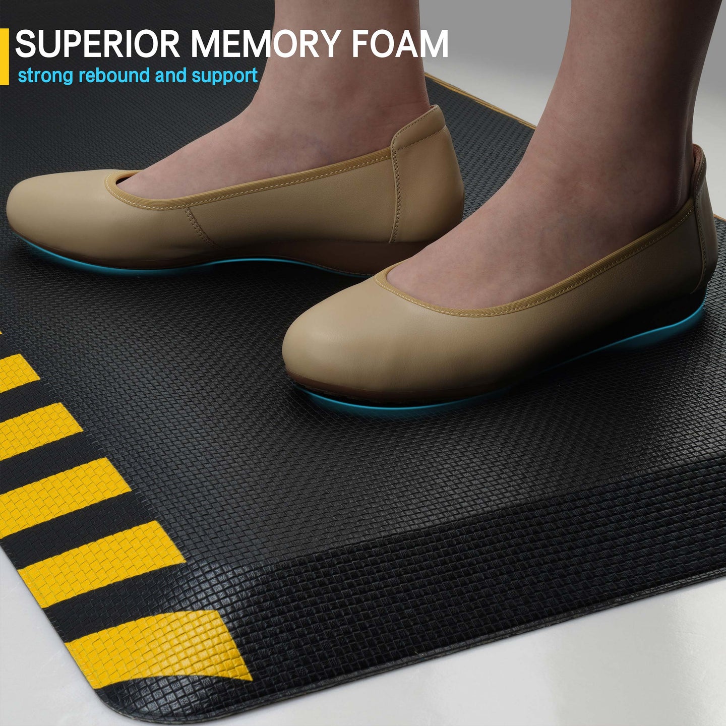 Close-up of feet in beige flats standing on black memory foam anti-fatigue mat with yellow striped border
