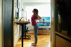 woman with back and neck discomfort at standing desk before using an anti fatigue floor mat